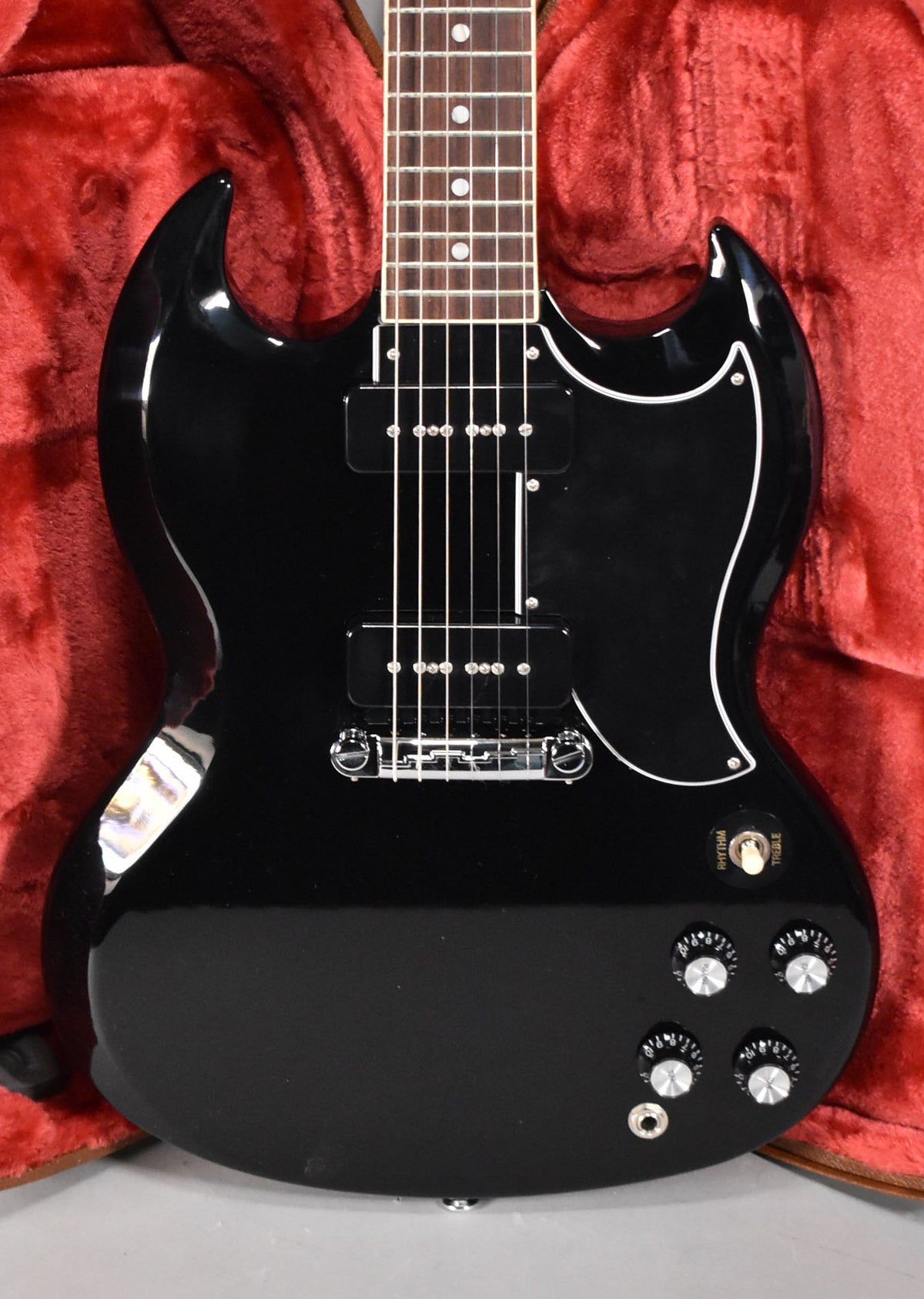 Full-frame, top-down view of a glossy black SG with a white pickguard, two P90 pickups, and four chrome-top knobs.