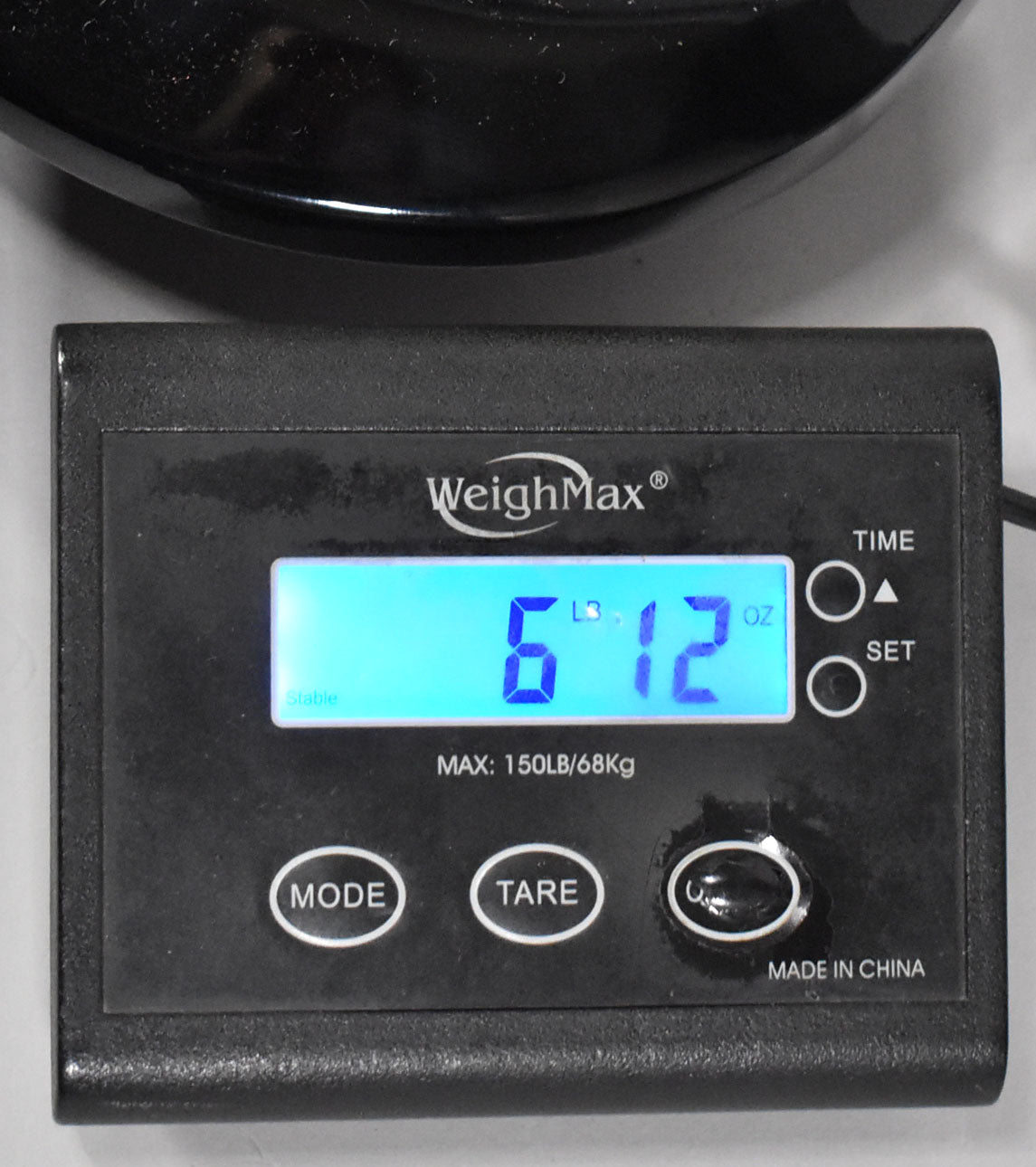 A close-up of a digital scale displaying "6 LB 12 OZ" in blue, with the guitar's black body partially visible above.