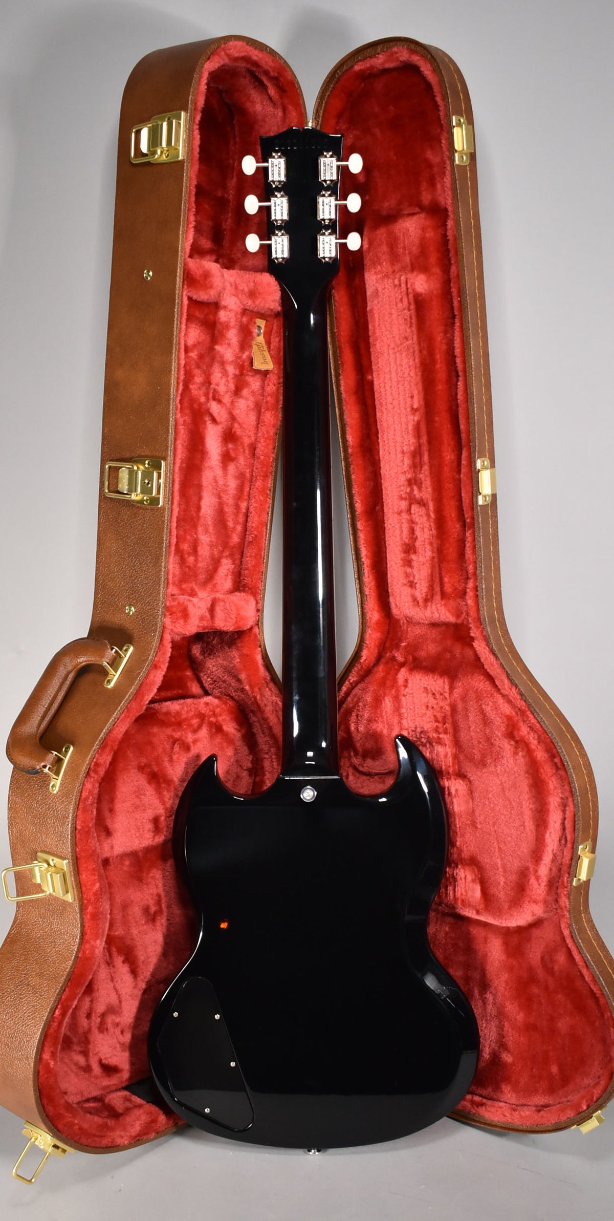 The back of a glossy black SG Special with white tuners, resting in a brown hardshell case with red plush lining.