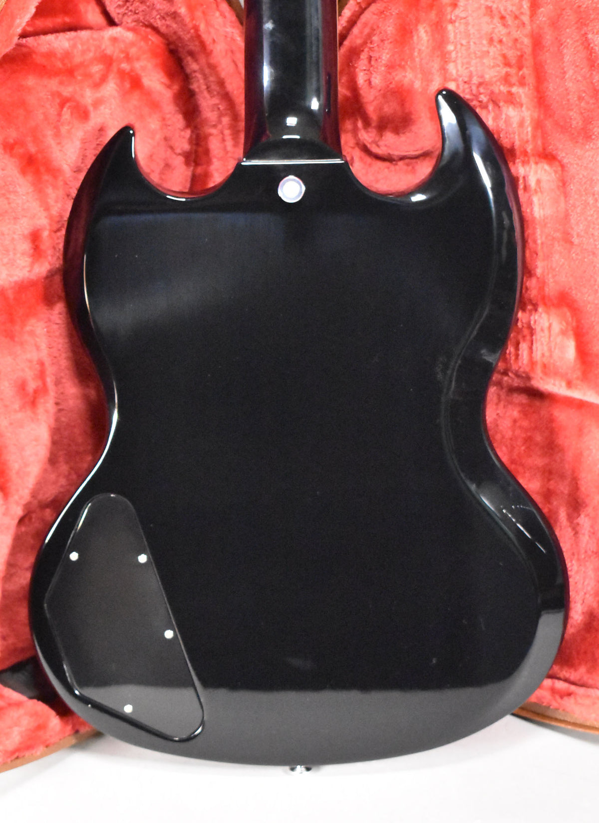 The back of a glossy black SG Special, showing the neck joint, strap button, and control cavity cover, in a red case.