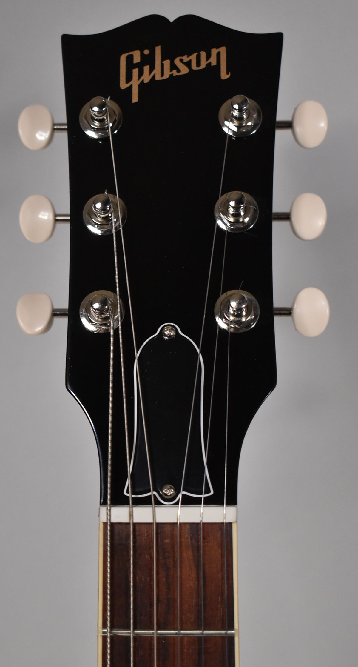 Close-up of the guitar's black headstock with cream tuning pegs, chrome tuners, and a white-outlined truss rod cover.