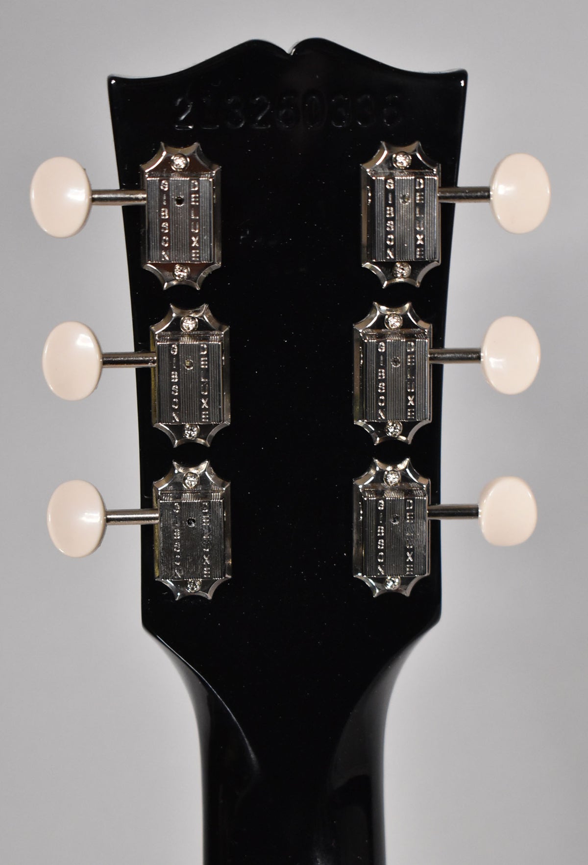 Rear view of the ebony headstock, showing six chrome tuners with cream buttons and a faint serial number at the top.