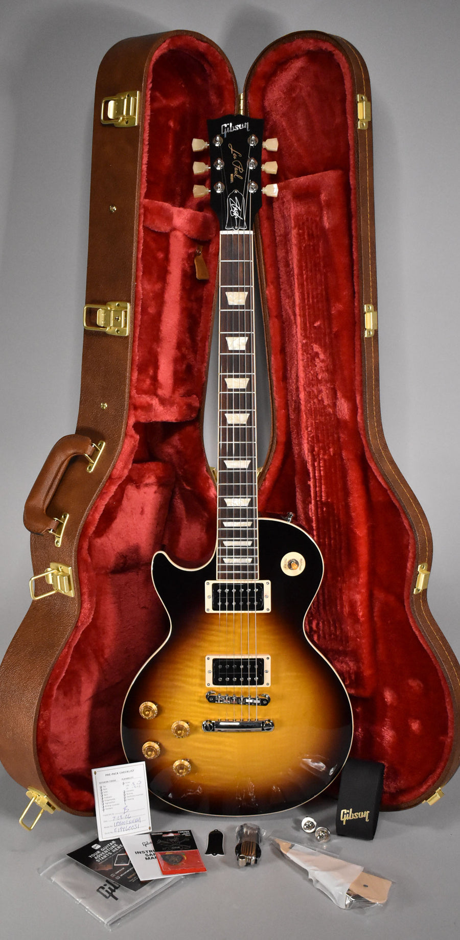 A full-length shot of a left-handed November Burst Les Paul in its brown hardshell case with red plush lining, surrounded by accessories.