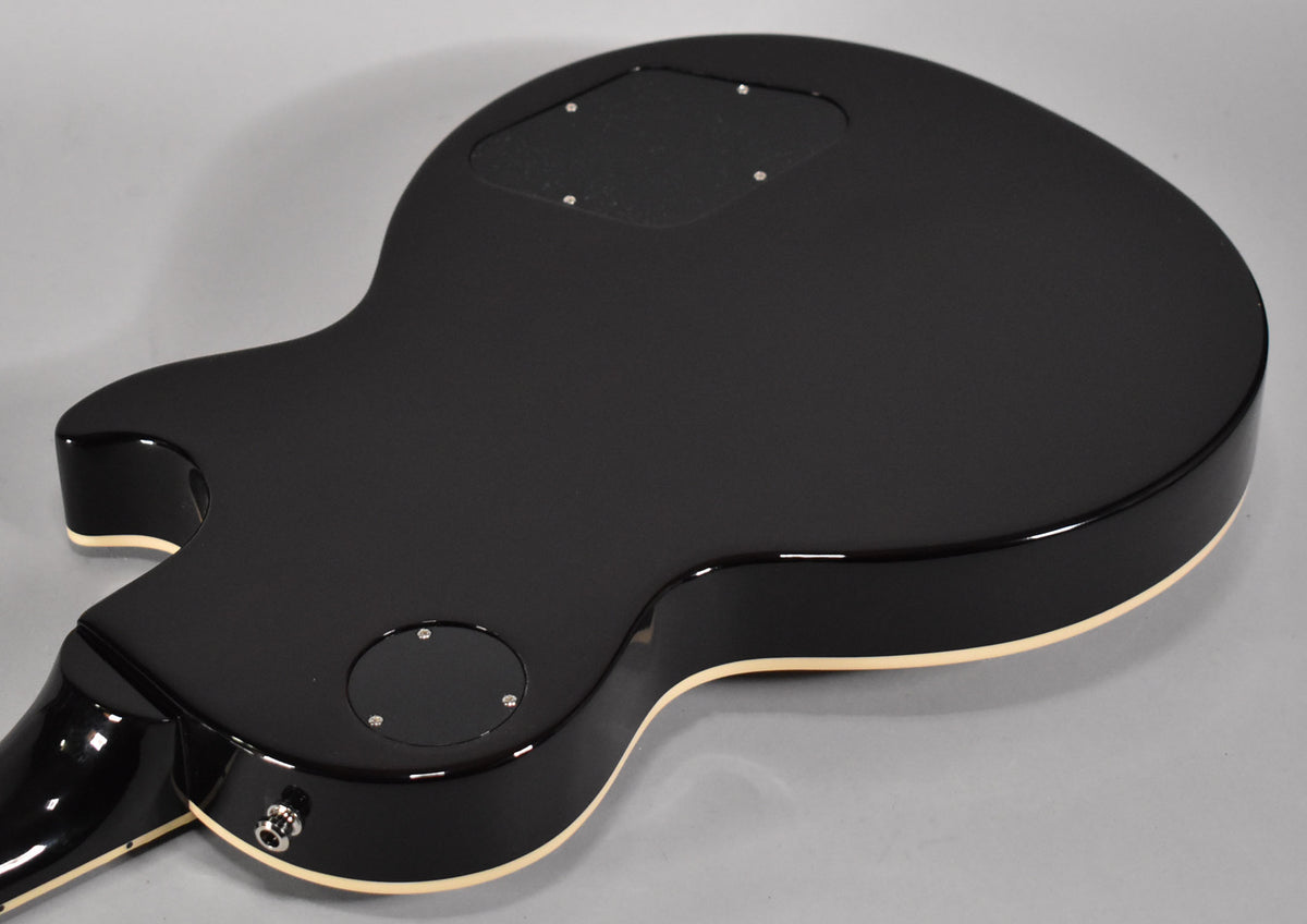 The back of the black Les Paul shows a matte finish on the body, gloss on the neck, and cream binding around the edges.