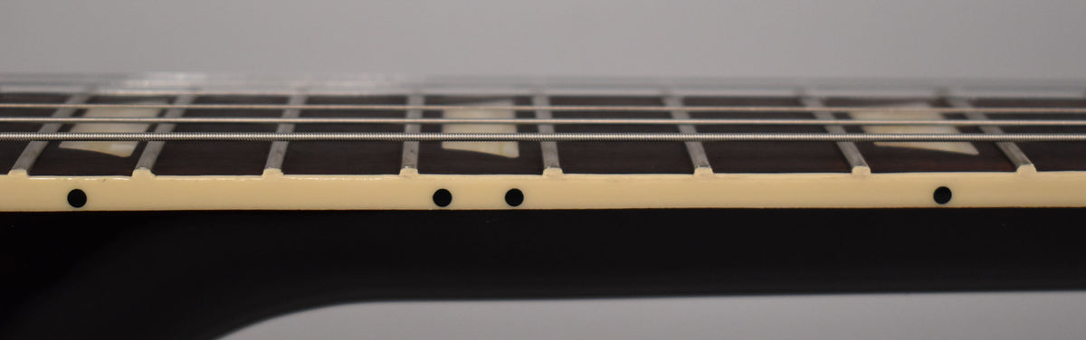 Close-up of the guitar's dark fretboard and cream binding, showing trapezoid inlays and side dots, with strings running across.