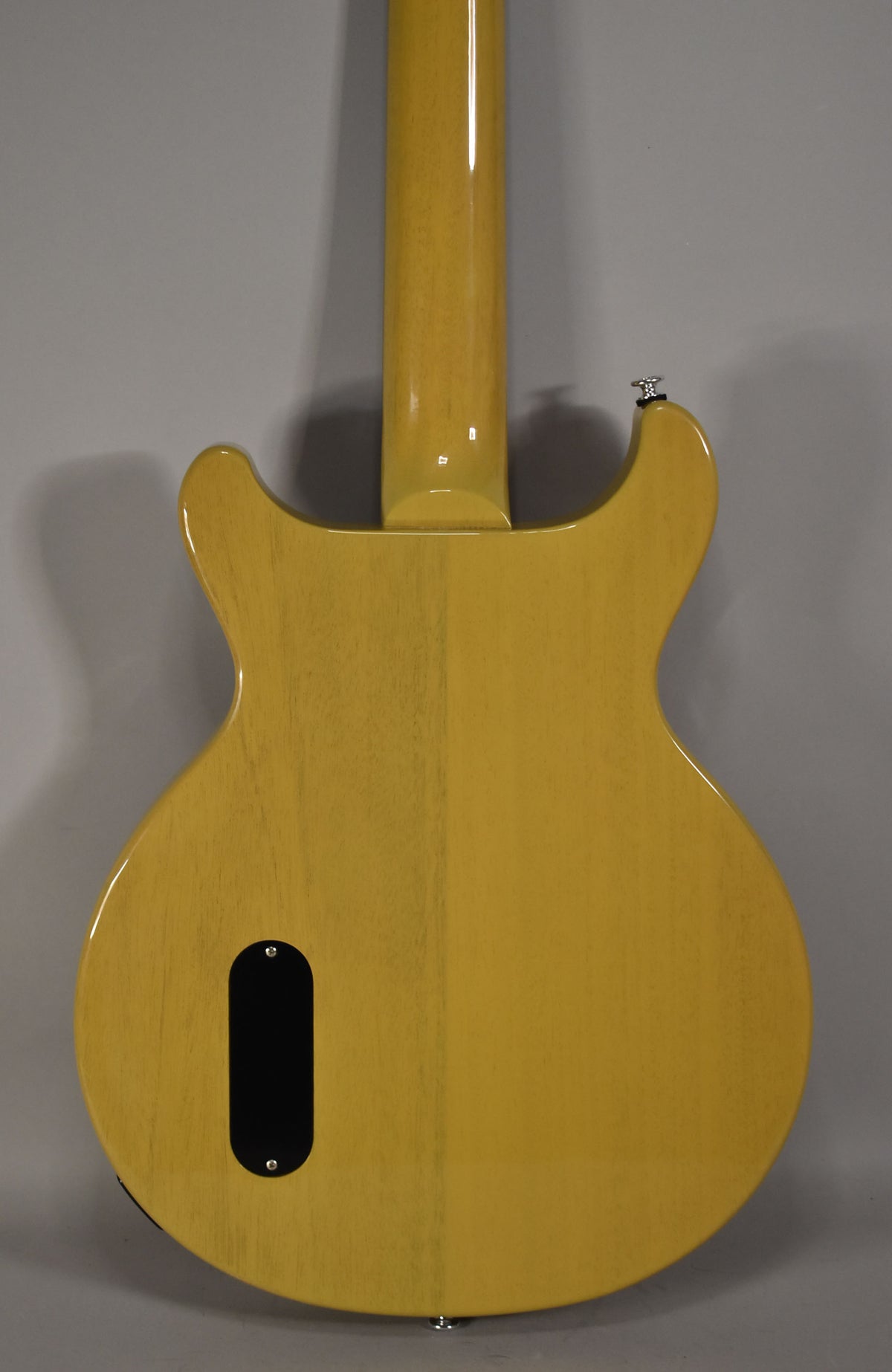 The back of a TV Yellow double-cut guitar, showing the neck joint, a black control cavity cover, and a strap button.