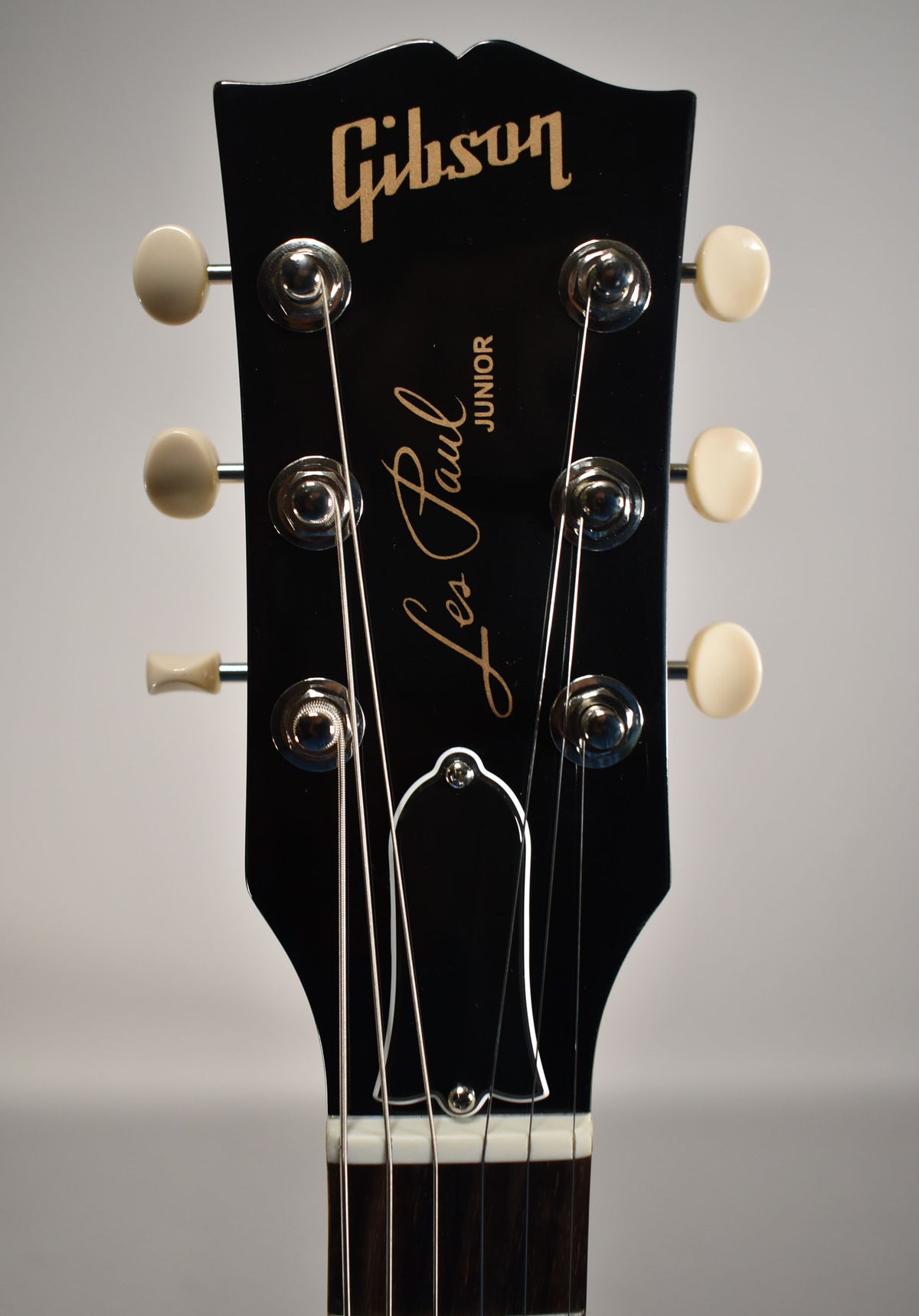 The black headstock, with a glossy finish, features six cream-colored tuning pegs and a bell-shaped truss rod cover.
