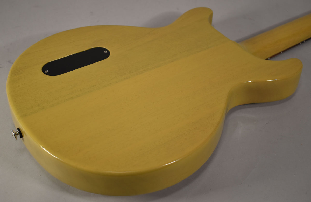 The back of a TV Yellow double-cut guitar, showing the grain through the finish, a black control plate, and a chrome strap button.