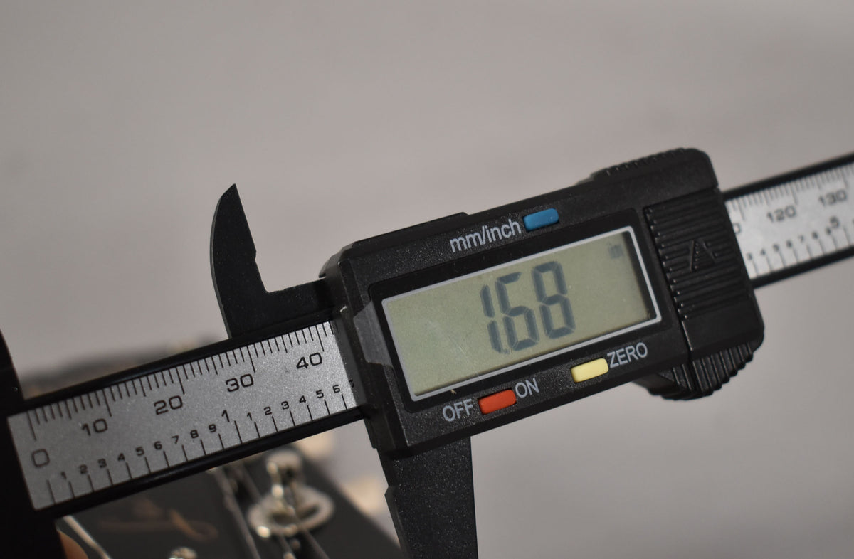 A digital caliper measures the guitar's nut width at 1.68 inches, with the headstock and tuning pegs visible below.