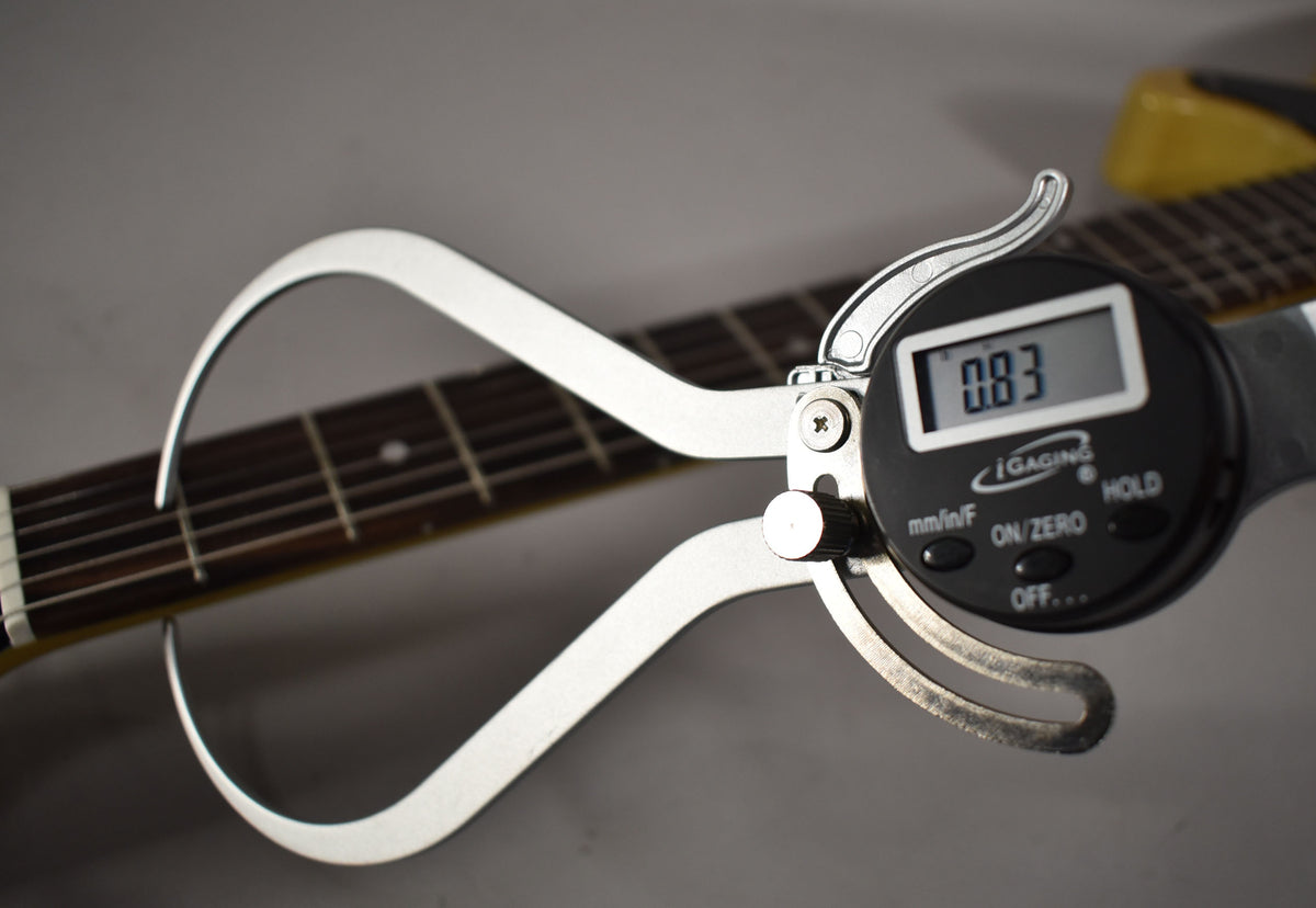 A digital caliper measures the guitar's fretboard, displaying "0.83" on its screen, with the TV Yellow body visible at the top right.