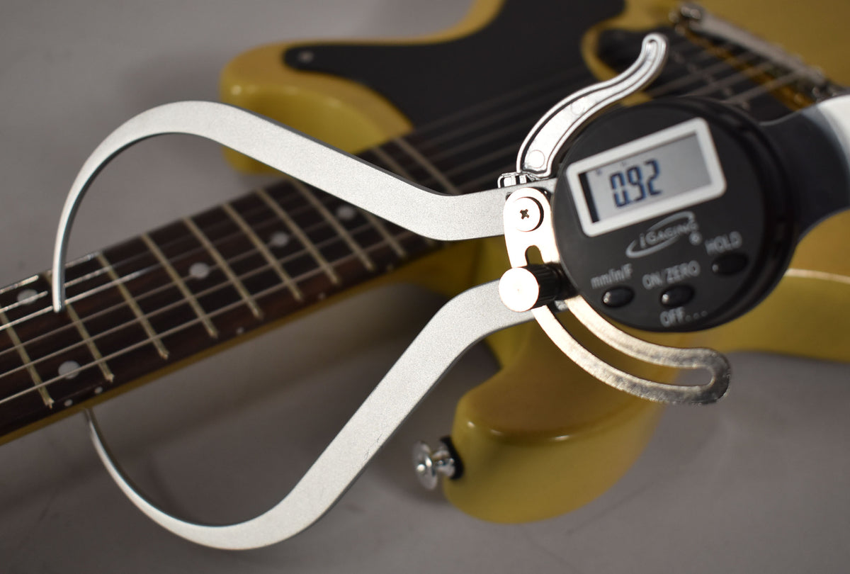 A digital caliper measures the guitar's fretboard, showing "0.92" on its screen, with the TV Yellow body blurred in the background.