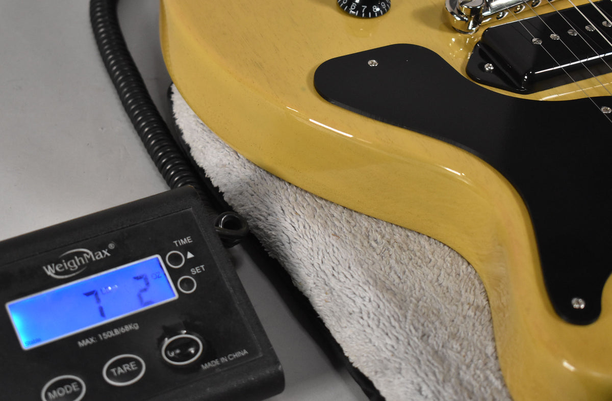Close-up of the TV Yellow guitar body on a scale, showing 7 lbs 2 oz, with a black pickguard and single P90 pickup.