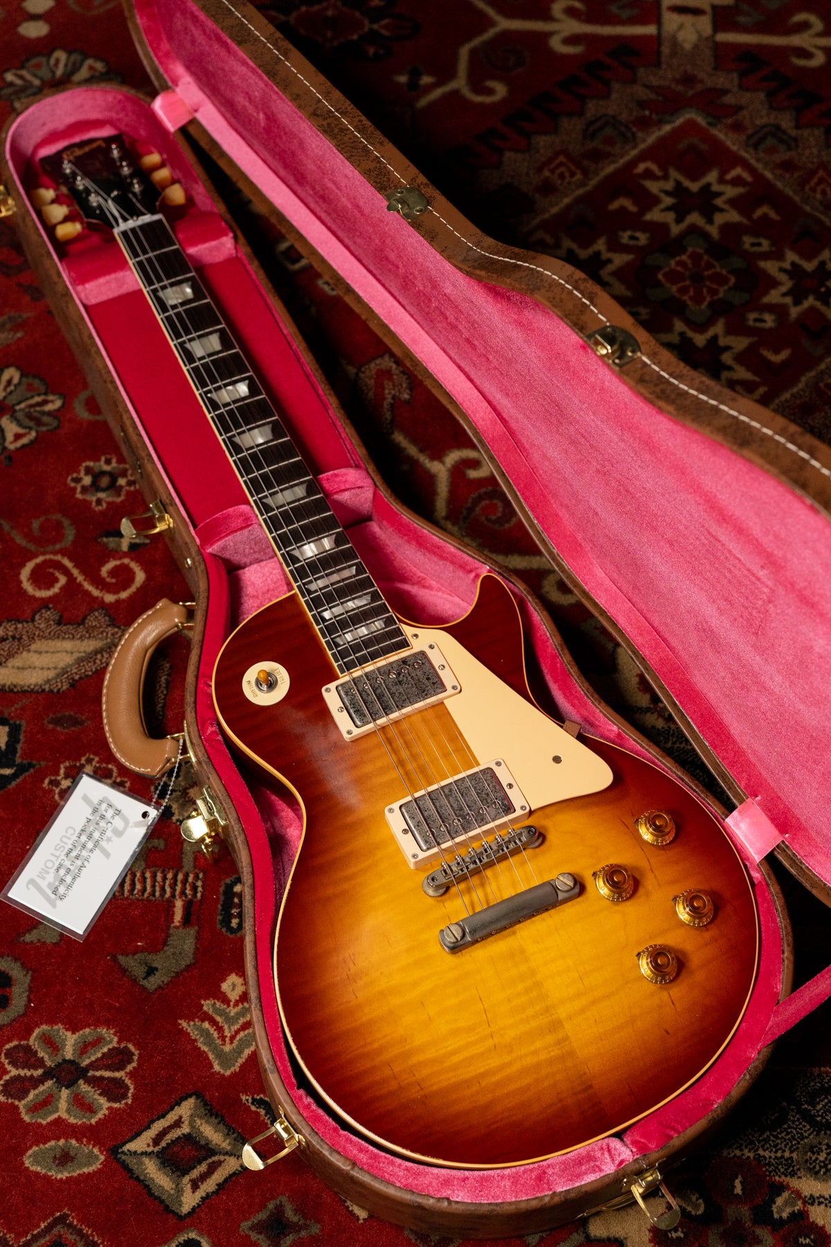 Sunburst Les Paul in a brown case with pink lining, angled from above, showing the full body and most of the neck.