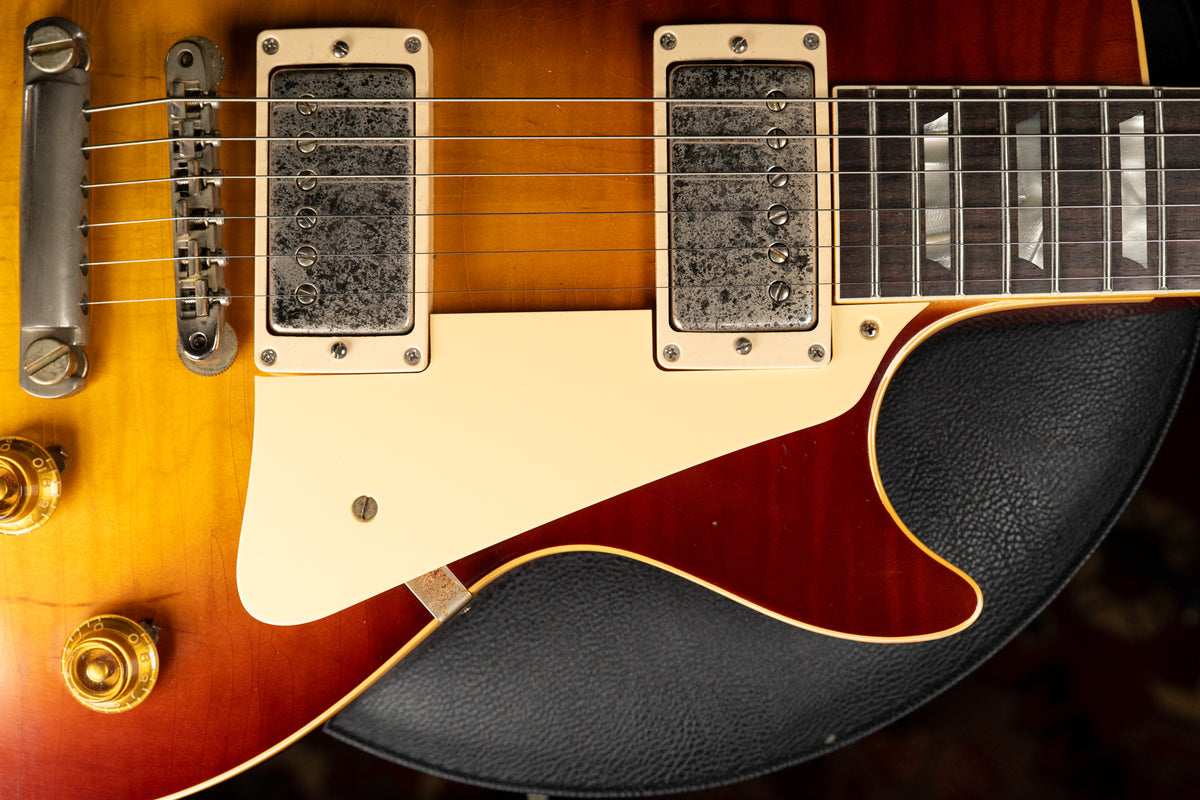 Close-up of the sunburst body, showing two aged humbuckers, a cream pickguard, gold control knobs, and trapezoid fretboard inlays.