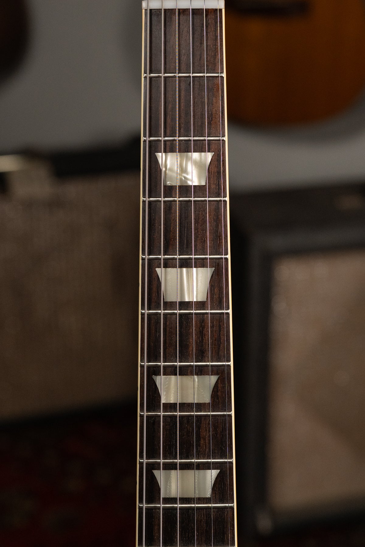 Close-up of the dark rosewood fretboard with trapezoid mother-of-pearl inlays, showing frets 1 through 7 and light string wear.
