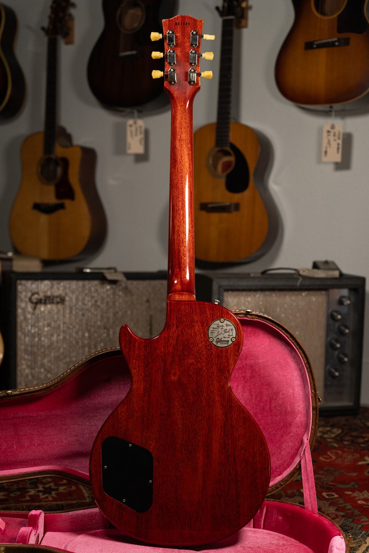 The back of a cherry sunburst Les Paul, with a dark red body and neck, is shown in a pink velvet-lined hard case.