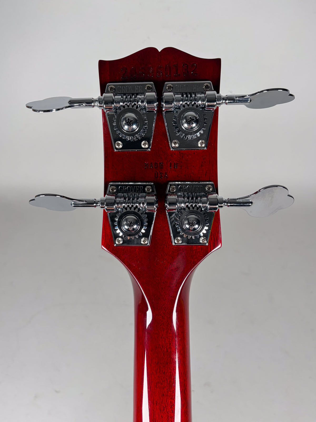 The back of a cherry red headstock and neck, showing four chrome tuning machines with clover-shaped buttons.