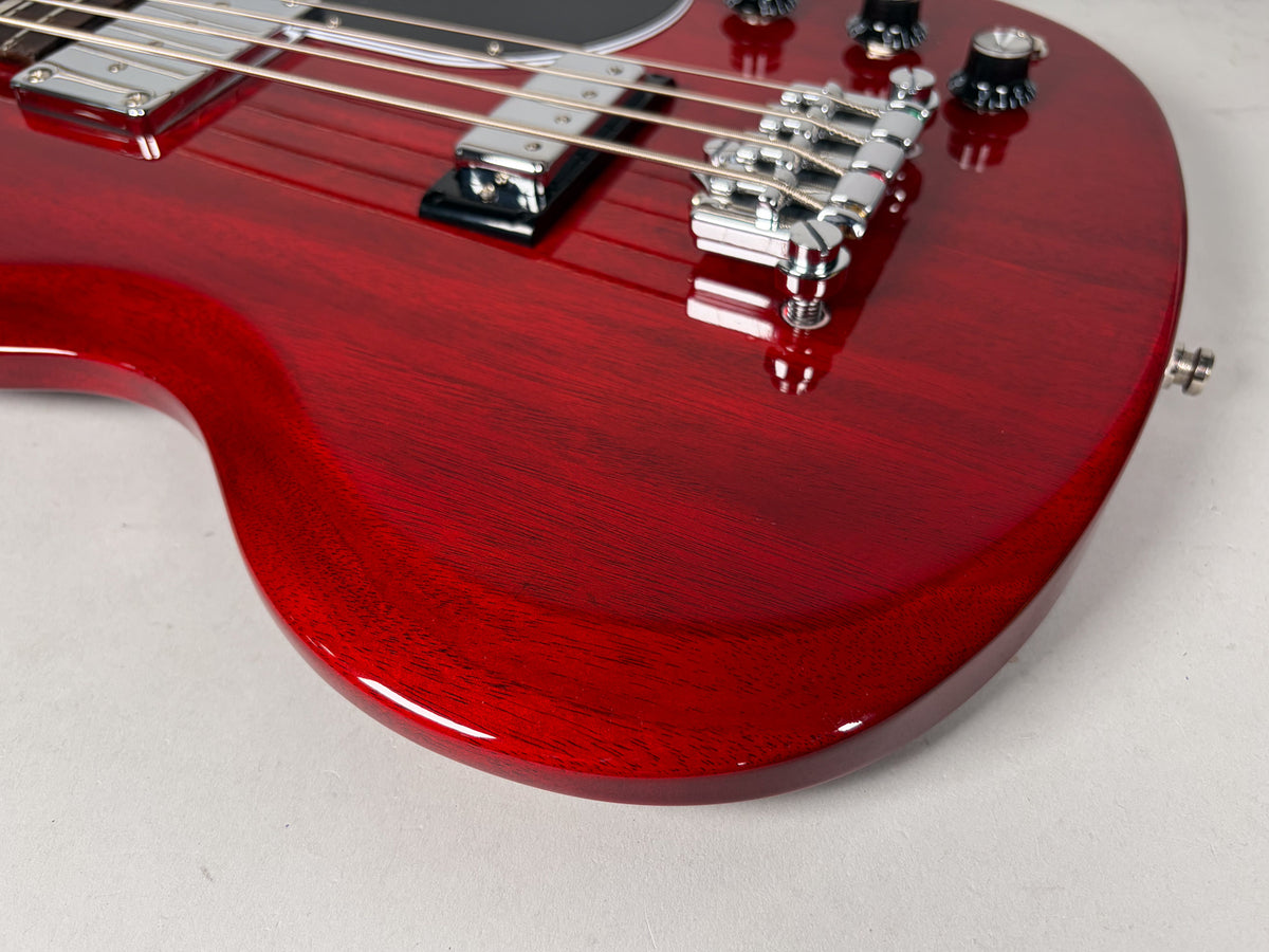 Close-up of the cherry red bass body, showing wood grain through the glossy finish, chrome bridge, two pickups, and control knobs.