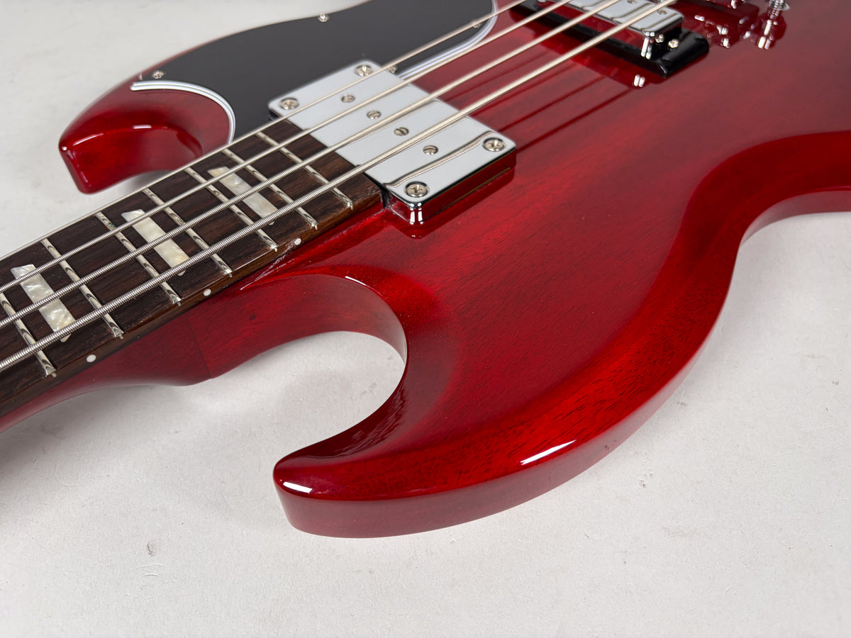 Close-up of the SG bass's cherry finish body and neck joint, showing the black pickguard, two chrome pickups, and trapezoid inlays.