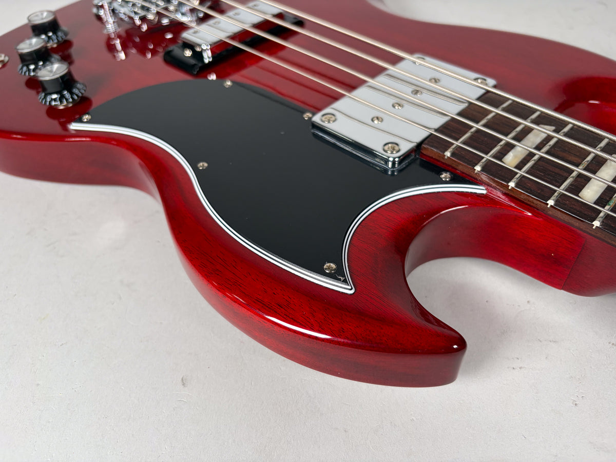 Close-up of the cherry red SG bass body, showing the black pickguard, chrome pickups, and three control knobs.