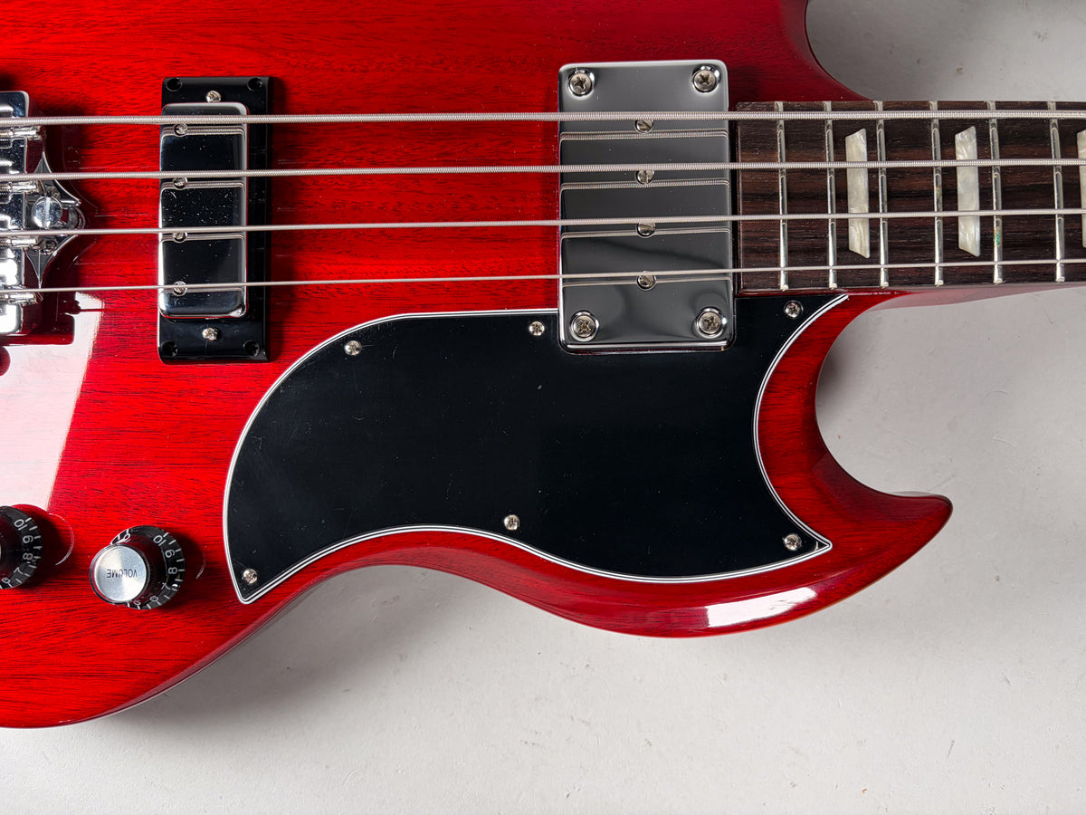 Close-up of the cherry red bass body, showing the black pickguard, two chrome pickups, volume/tone knobs, and the fretboard with block inlays.