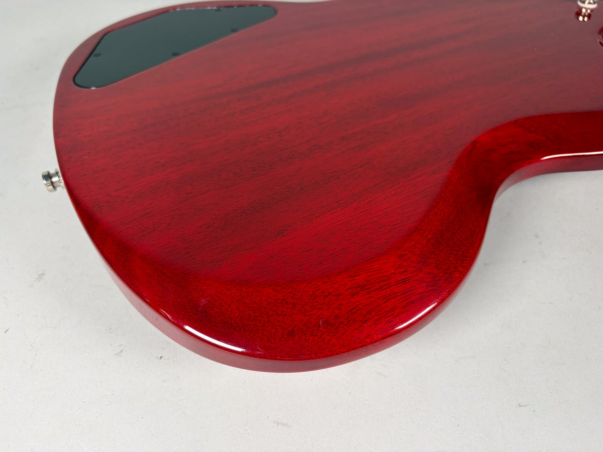The back of the cherry red bass body, showing the control cavity cover, output jack, and a small ding on the lower bout.