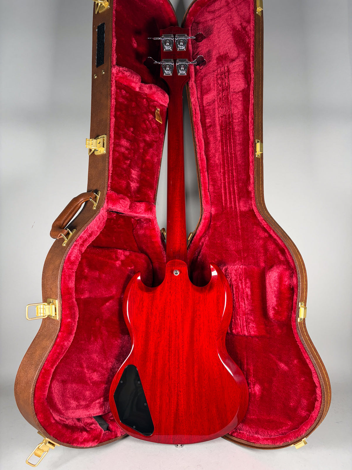 The cherry finish bass is shown from the back, resting in its open brown hardshell case with red plush lining.
