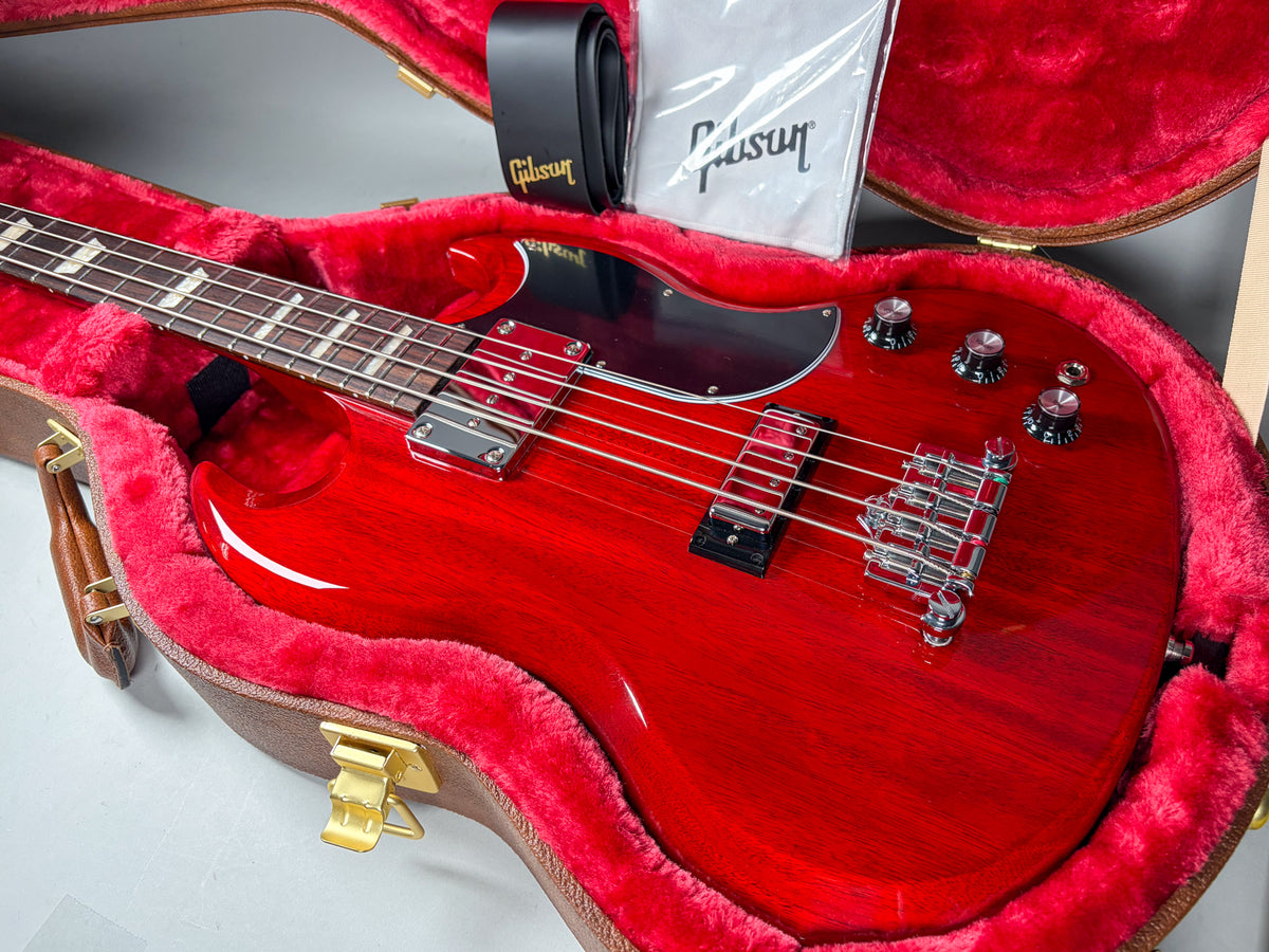 Cherry red bass in a brown hard case with red plush lining, showing the body, neck, and headstock from above.