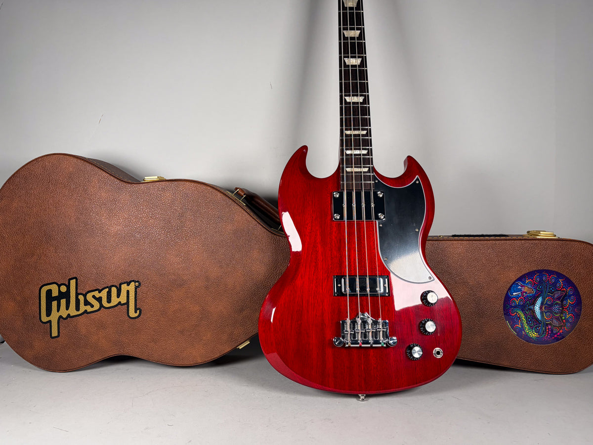 Red Gibson SG bass guitar with two brown cases, one with a Gibson logo, the other with a colorful circular sticker.