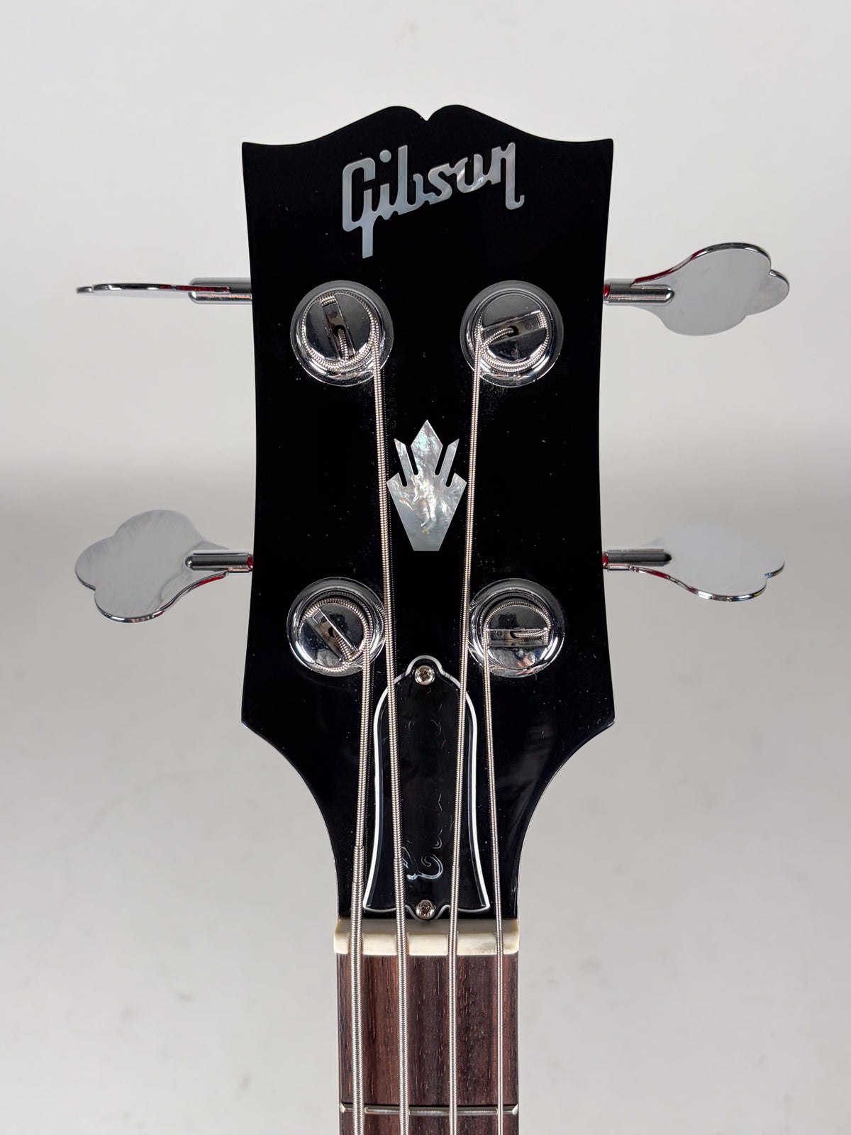 Close-up of the black headstock with four chrome clover-leaf tuners, a mother-of-pearl crown inlay, and a bell-shaped truss rod cover.