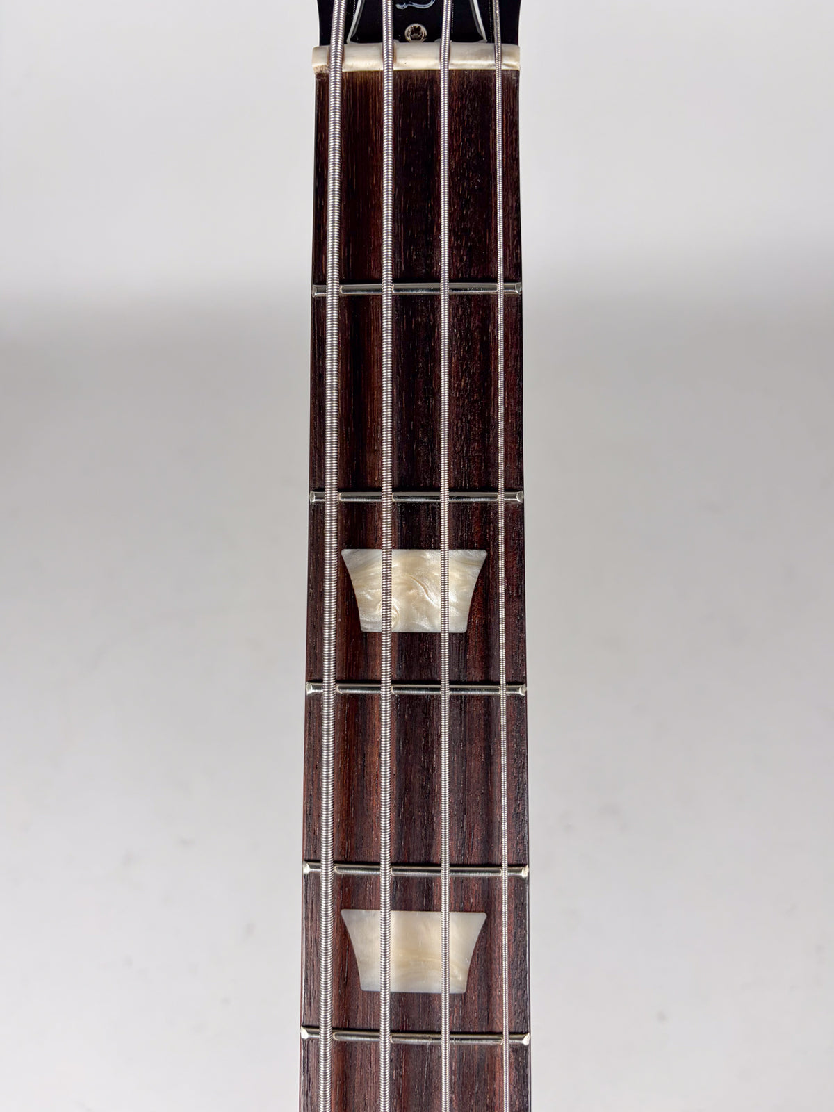 Close-up of the dark rosewood fretboard with trapezoid mother-of-pearl inlays, four strings, and silver frets.