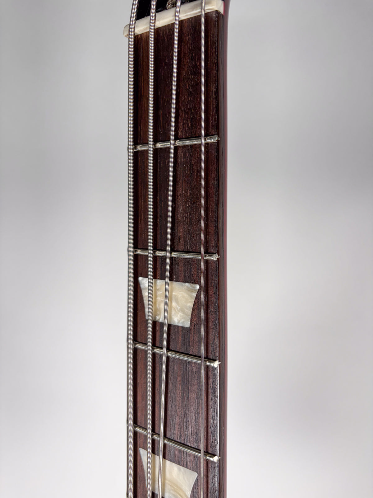 Close-up of the dark rosewood fretboard with trapezoid mother-of-pearl inlays and four silver strings over a white nut.