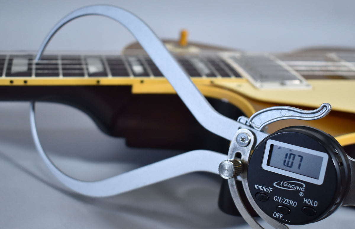 A digital caliper measures the guitar's neck relief at 1.07, with the dark brown neck and cream binding visible in the background.