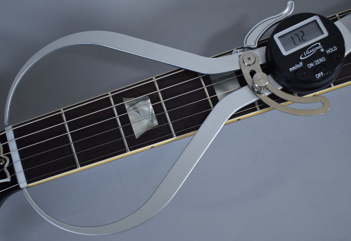 A digital caliper measures the dark fretboard with trapezoid inlays, displaying "1.72" on its screen.