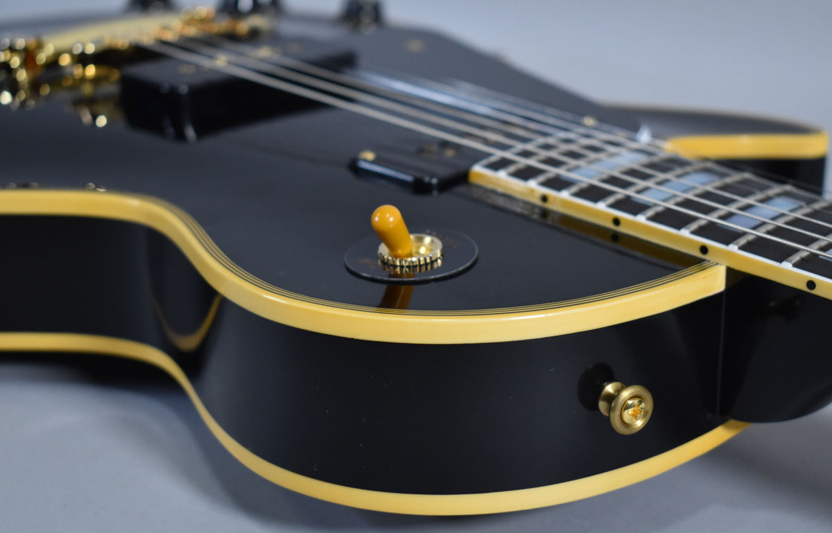 Close-up of the glossy black body, showing the cream binding, gold hardware, amber switch tip, and part of the fretboard.