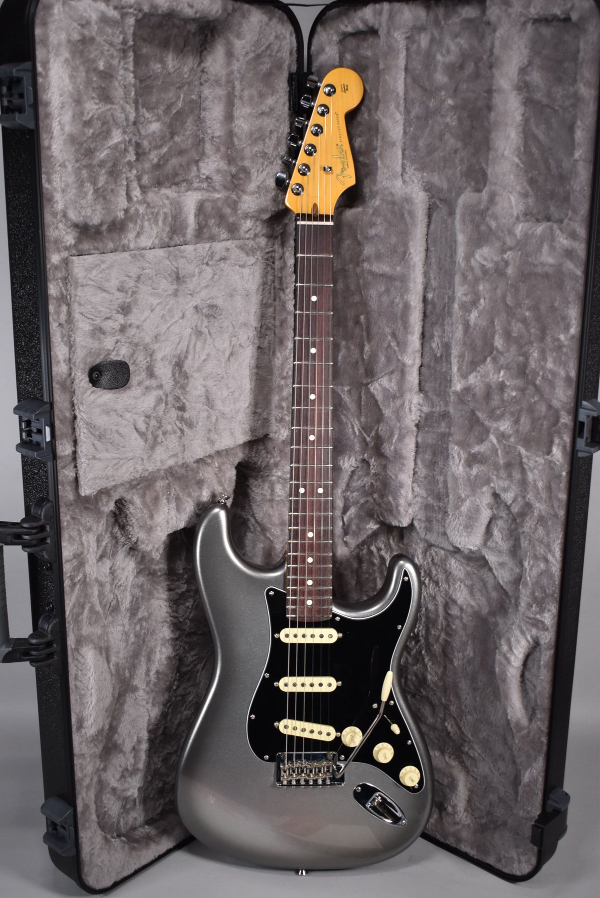 Full-length view of a metallic silver Stratocaster with a black pickguard, cream pickups and knobs, in a plush grey hard case.