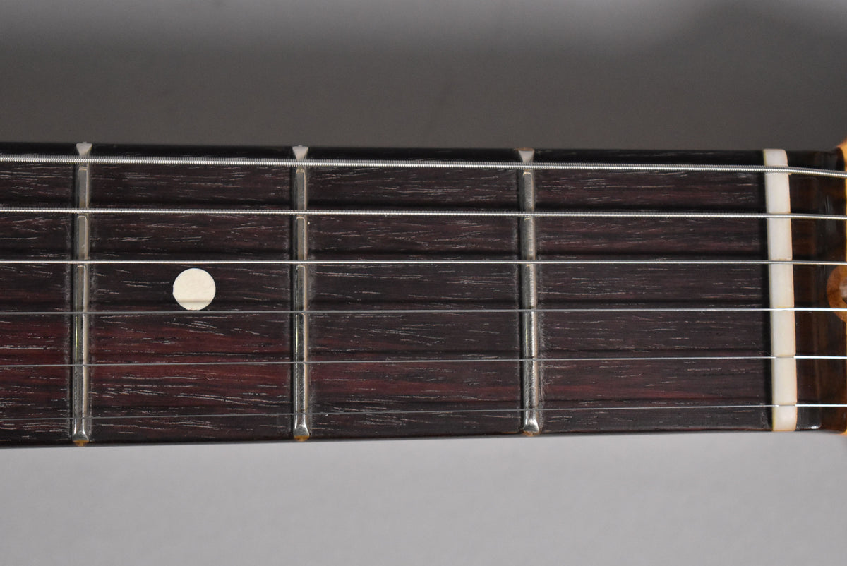 Close-up of the dark rosewood fretboard with six strings, metal frets, and a single white dot inlay on the fifth fret.
