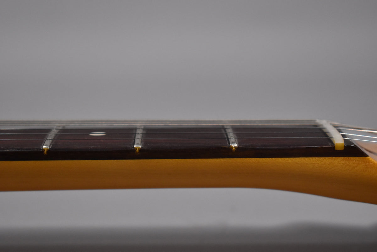Close-up of the guitar's dark fretboard and light-colored neck, showing frets, strings, and a white nut from a side angle.