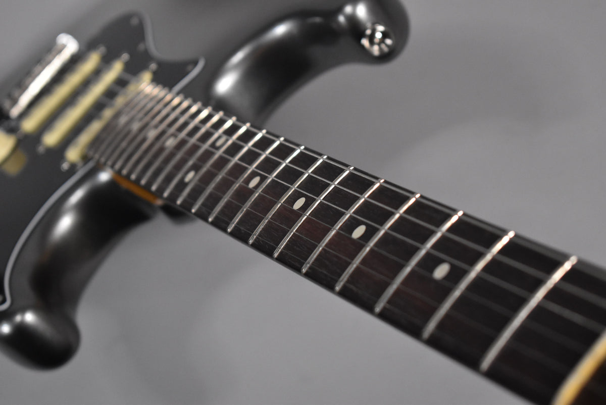 Close-up of the dark rosewood fretboard with white dot inlays and shiny frets, angled from the body towards the headstock.