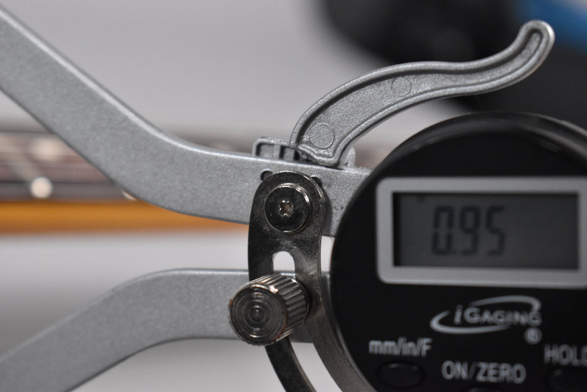 A close-up of a digital caliper measuring the guitar's fretboard, displaying "0.95" on its screen.