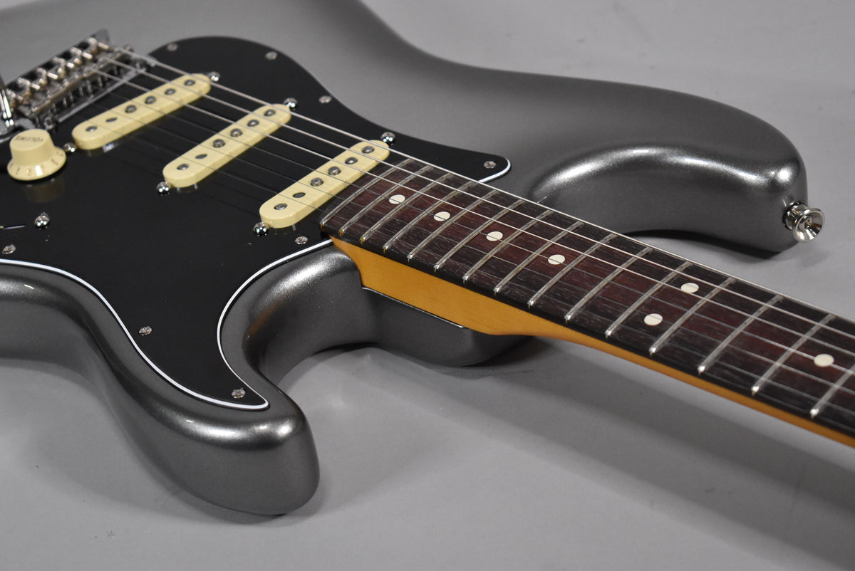 Upper body of a metallic gray Stratocaster with a black pickguard, cream pickups, and a dark fretboard with white dot inlays.