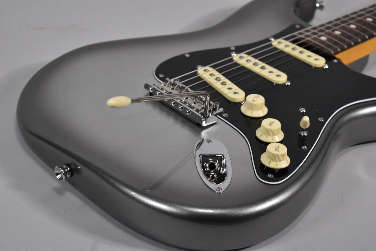 The Stratocaster's metallic mercury finish body is angled, showing the black pickguard, three cream single-coil pickups, and matching control knobs.