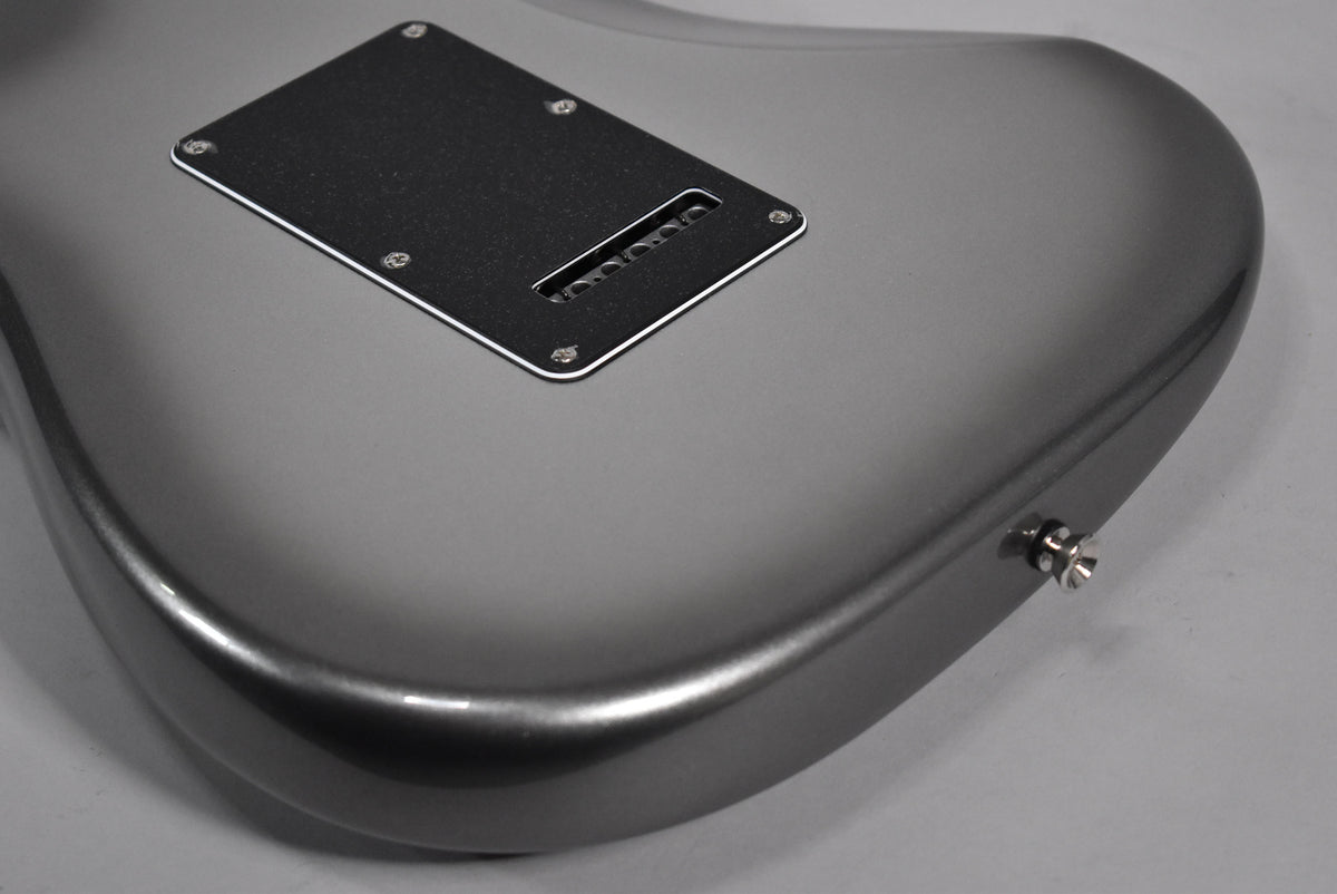 The back of a metallic gray electric guitar, showing the tremolo spring cover and output jack.
