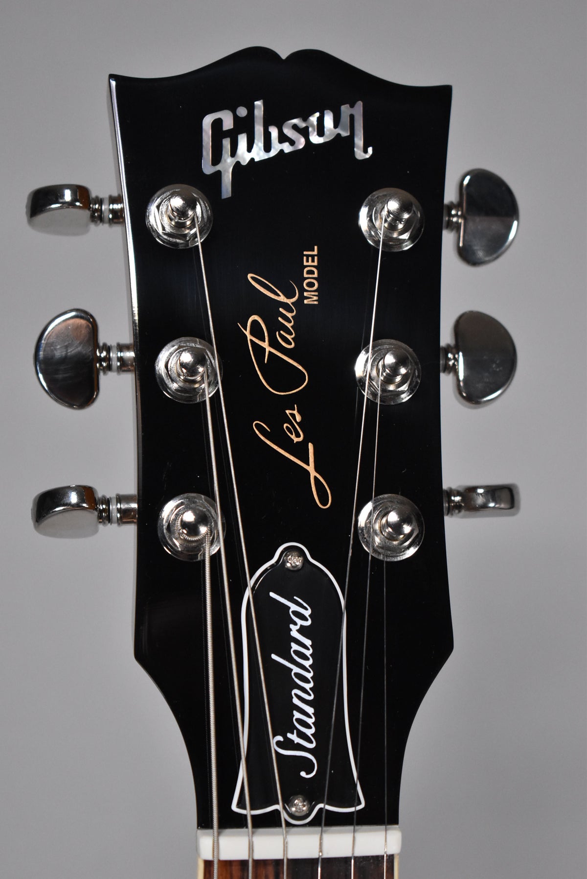 Close-up of the glossy black headstock with pearl inlay, showing six chrome tuning pegs and the top of the nut.