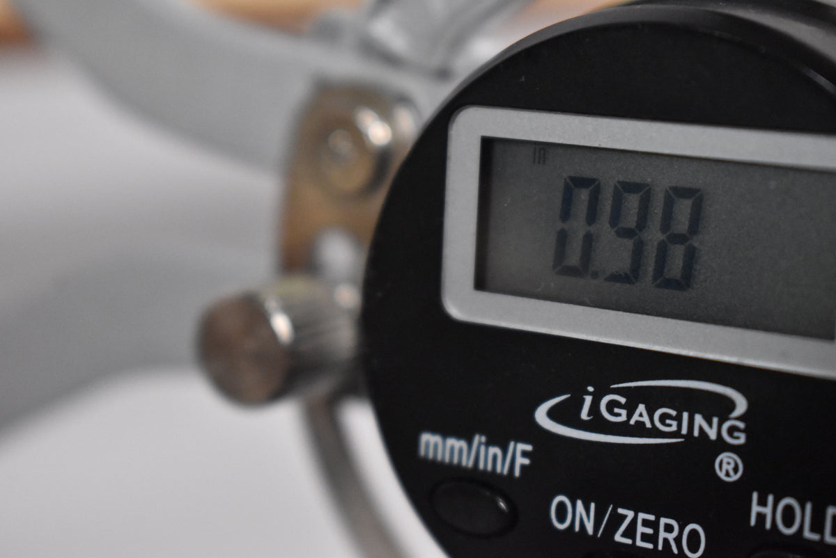 Close-up of a digital caliper showing a measurement of 0.98 inches, likely measuring the guitar's nut width or fret height.
