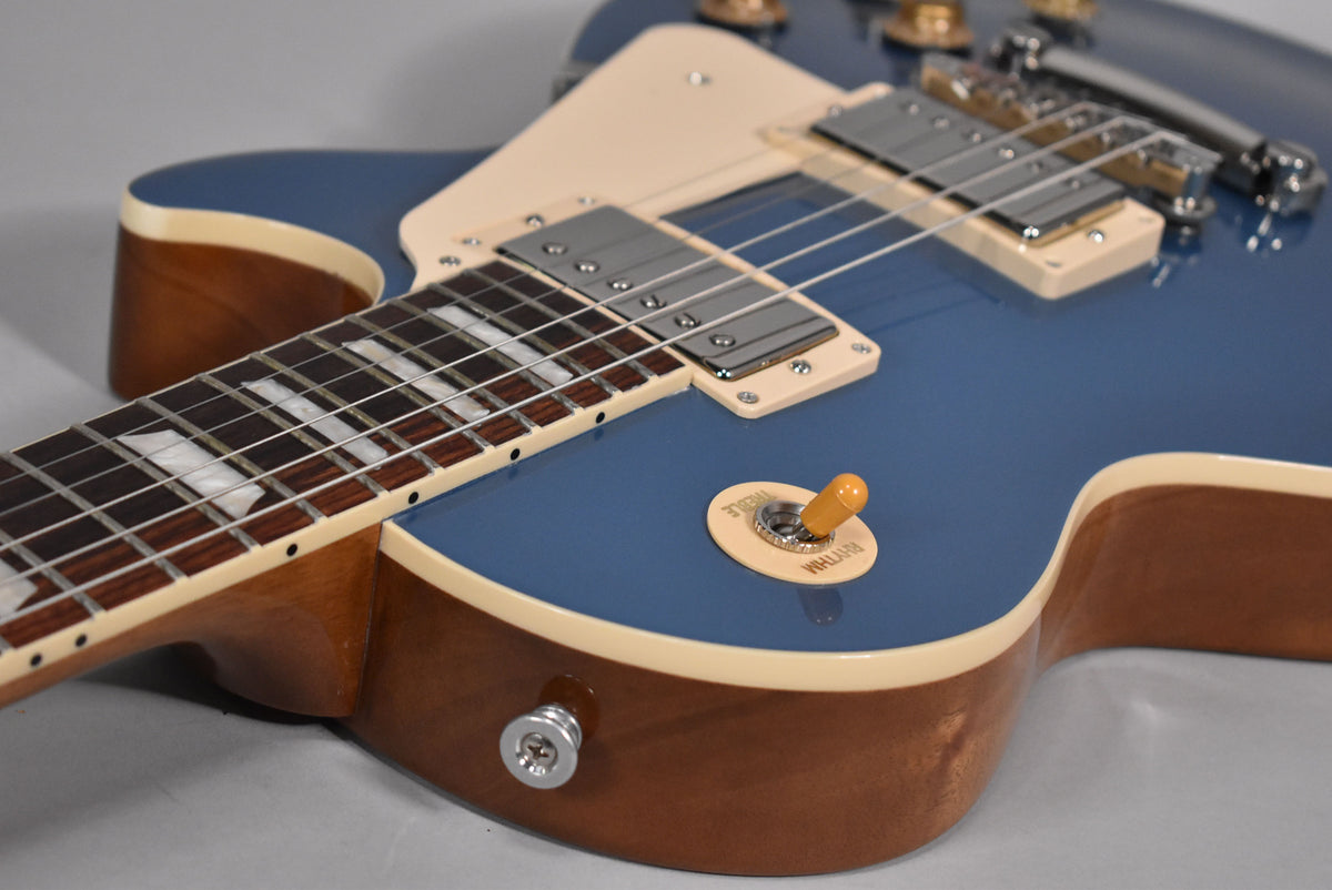 Close-up of a Pelham Blue electric guitar body, showing the neck, two humbucker pickups, and a cream toggle switch.