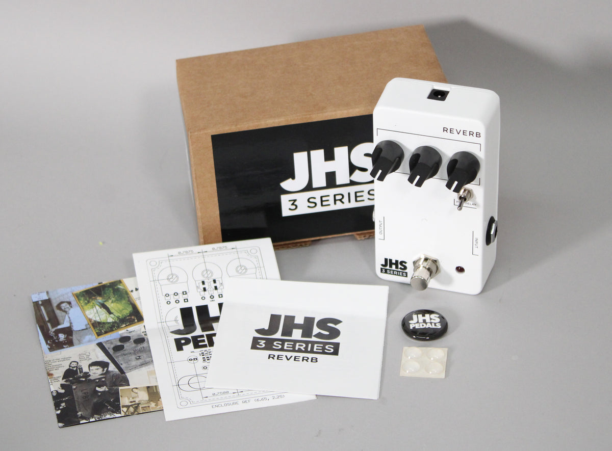 White reverb pedal with three black control knobs, a toggle switch, and a footswitch, shown with its box and paperwork.