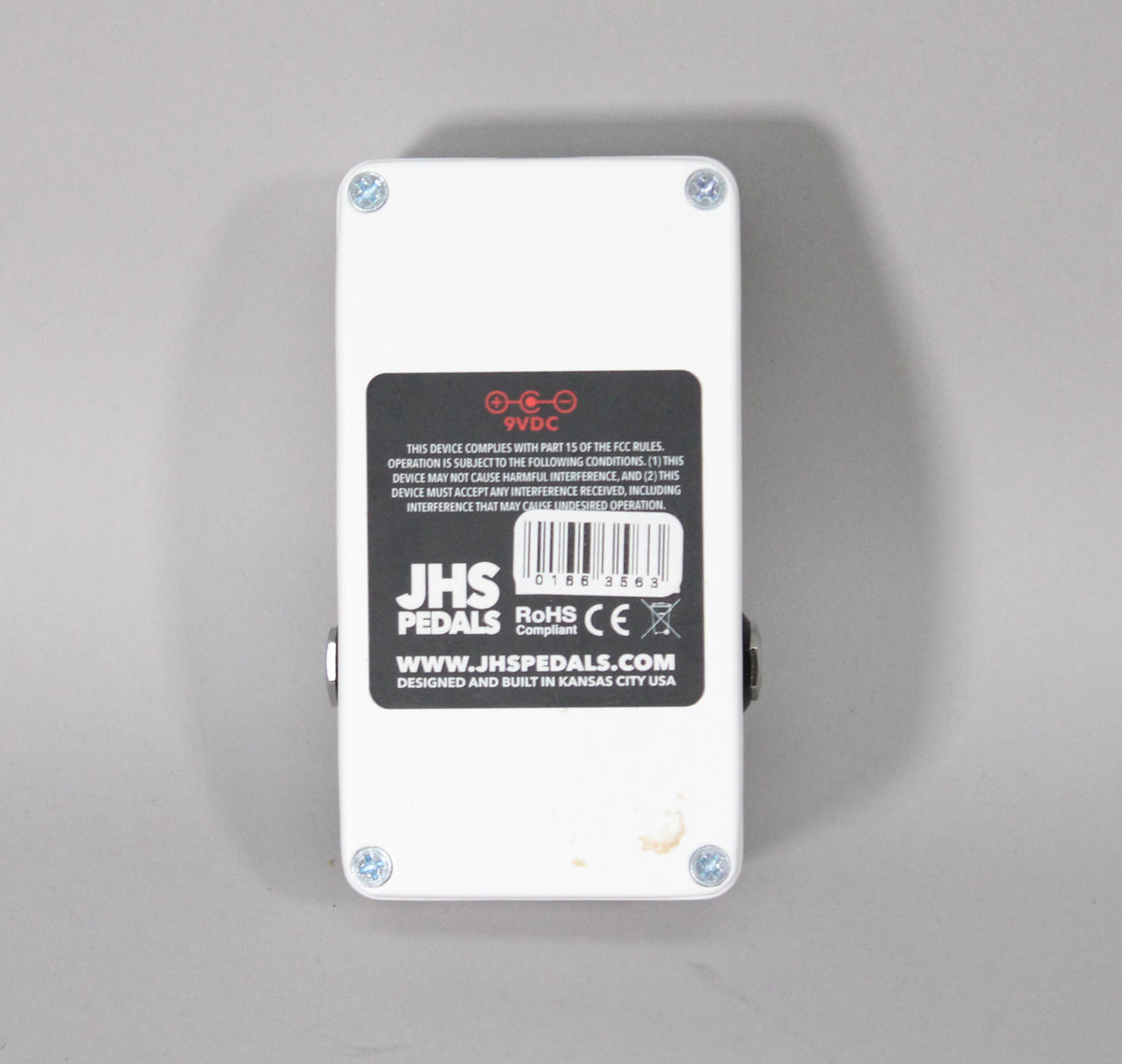 The white reverb pedal is viewed from the back, showing a black label and four silver screws, with minor scuffs.