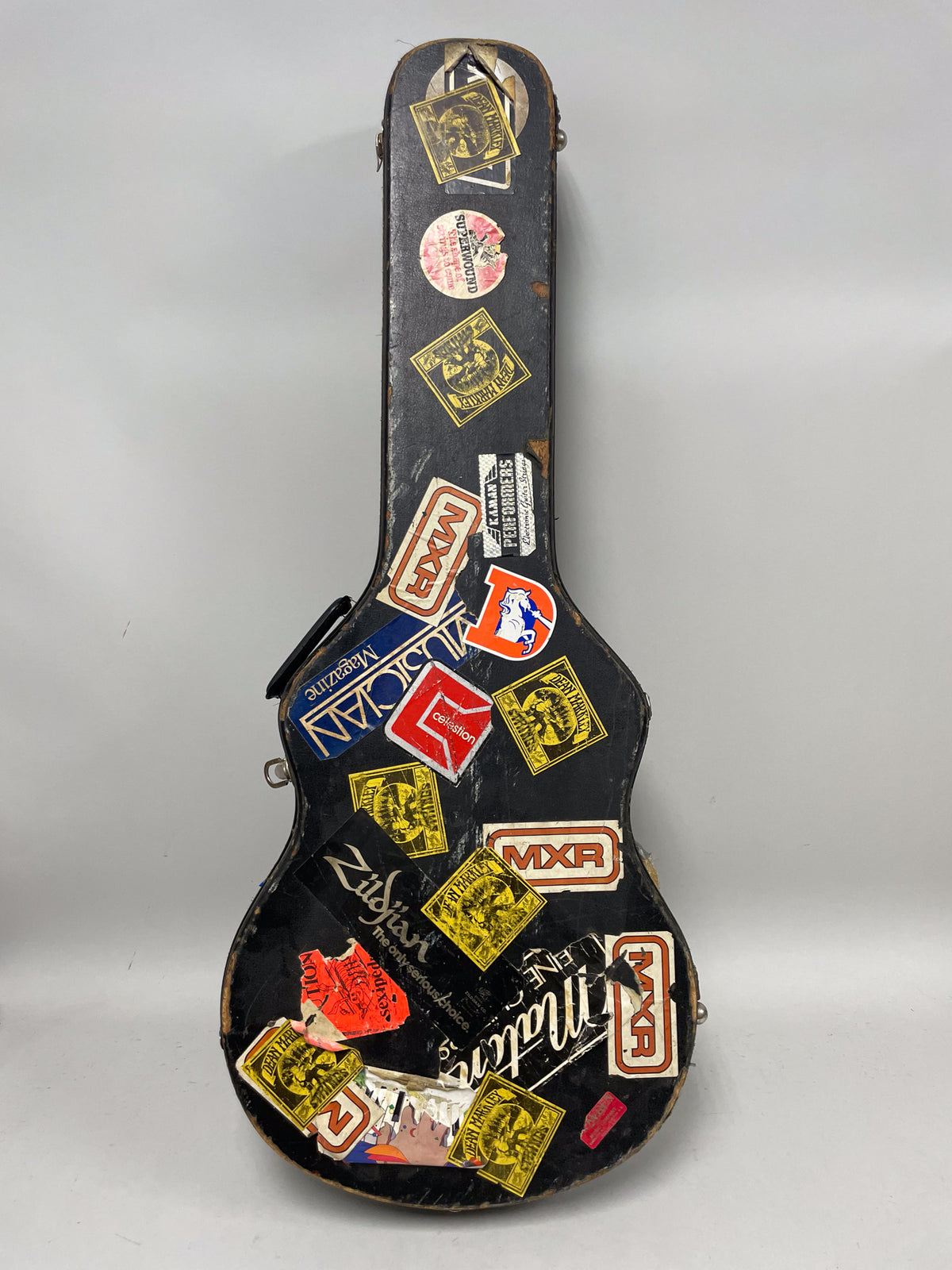 Full-length view of a black hard shell guitar case covered in many colorful, worn, and peeling stickers.