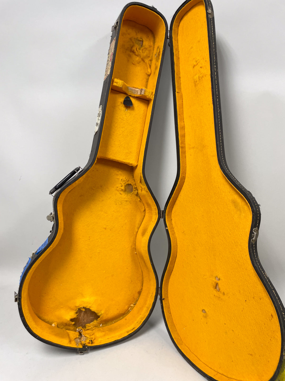 Open black guitar case with worn yellow plush lining, showing significant tears and exposed wood at the bottom.